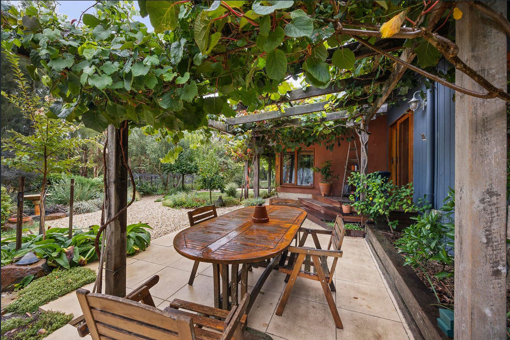 Outdoor patio with wooden table and lush greenery.